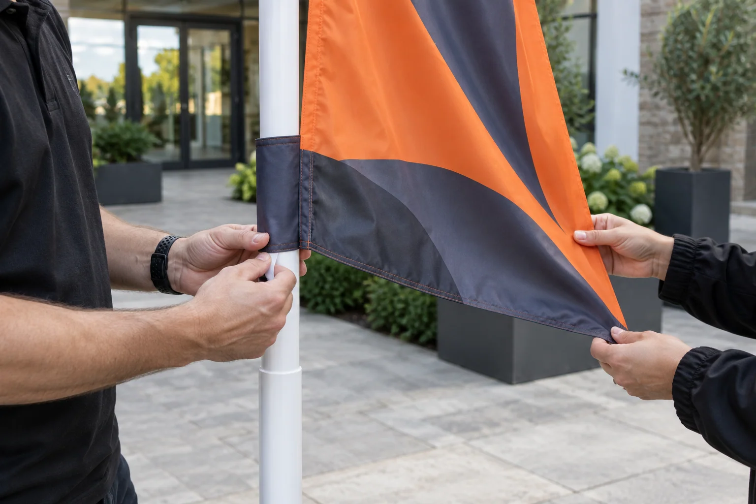 Hands inspecting a small orange and graphite flag wrapped around a white pole